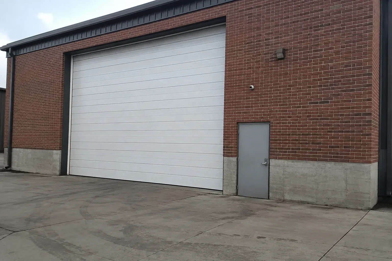 Tall closed sectional loading door beside a personnel door at a brick unit. — Commercial Sectional Door Repair, Orangeville