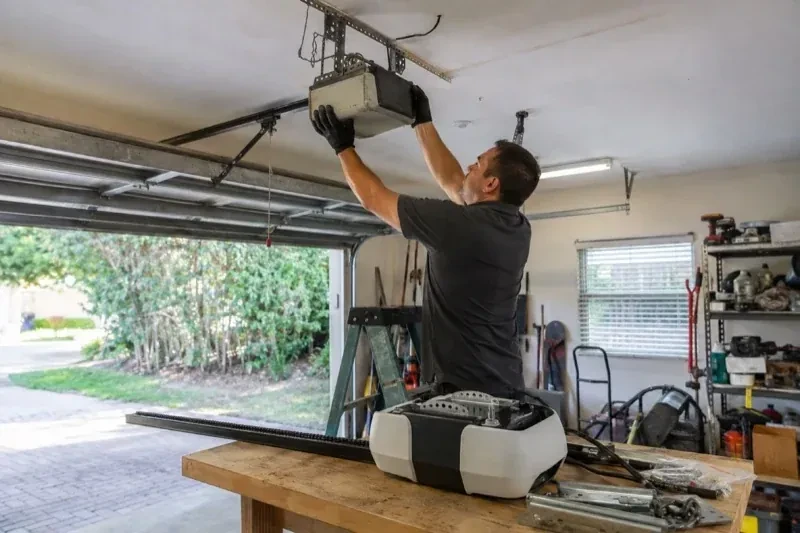 Person holding an overhead garage-door opener beside another opener and hardware on a workbench — Garage Door Opener Replacement, Orangeville