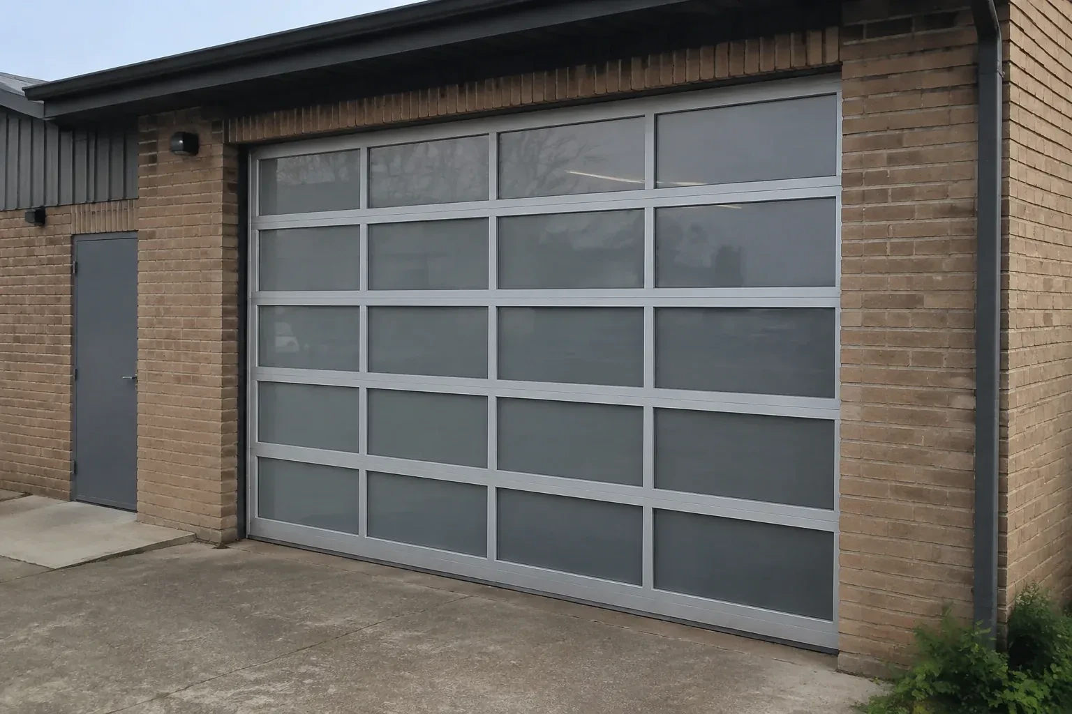 Closed glazed sectional door in a grey metal frame at a brick workshop. — Full-View Glass Garage Door Installation, Orangeville